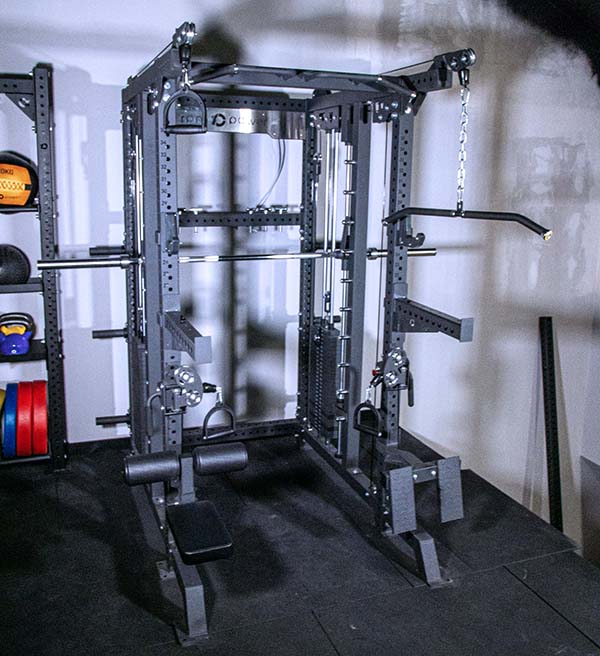 Multigym Tyr Rack with pull up handles, low row, spotter arms and footrest, beside the rack is weight plates, wall balls and slam balls